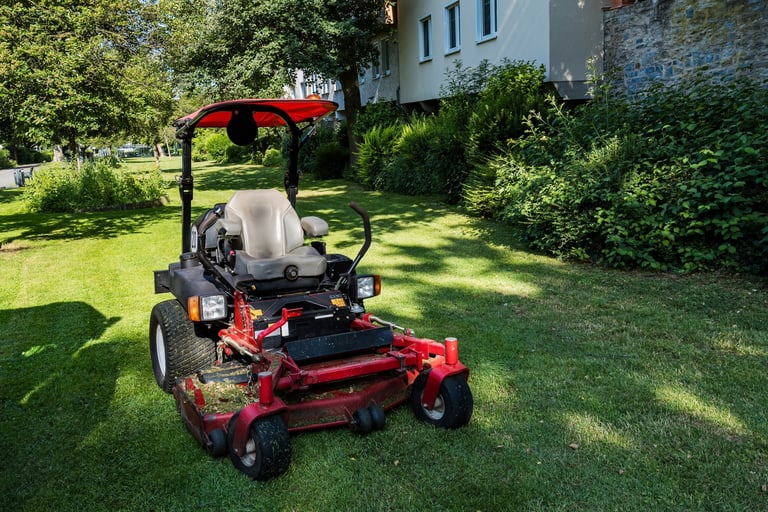 A riding mower parked on freshly cut grass in a residential area with green lawns and surrounding trees